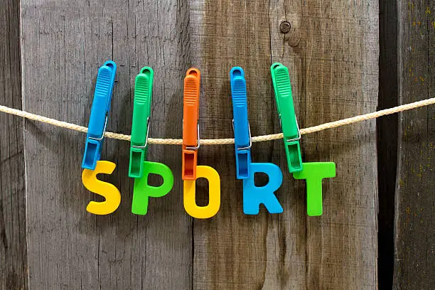 word sport fasten clothespins on a rope behind a wooden background