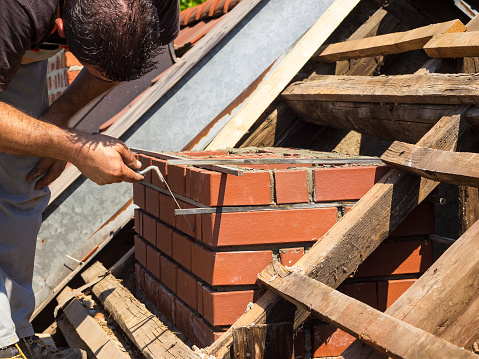 Man is measuring mortar thickness on chimney for new line of bricks on an old house in Ljubljana, Slovenia