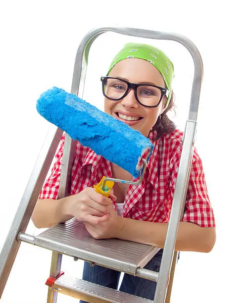 Smiling girl on ladder with roller ready for renovating or wall painting, isolated on white