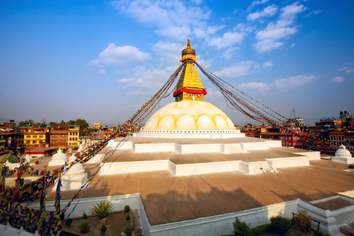 The iconic mandala dome of Boudhanath stupa, spotlit beneath dramatic sunset skies as crowds of pilgrims and tourists walk around the ancient Buddhist shrine, a UNESCO World Heritage Site in Kathmandu, Nepal's vibrant capital city.
