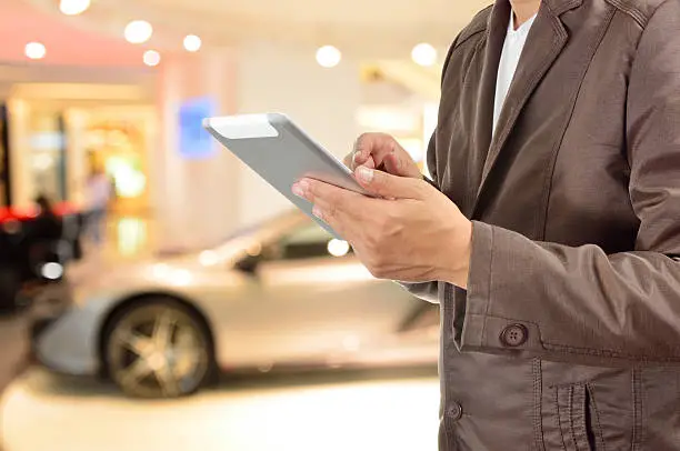 Young BusinessMan using Tablet device with Modern Sportcar as Modern Lifestyle Concept.  Selective Focus on Right hand Trigger finger .