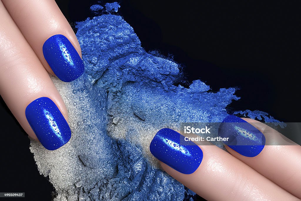 Blue Nail Polish and Mineral Eye Shadow Fashionable blue nails with drops of water and crushed eyeshadow in blue silver. Manicure and makeup concept. Closeup image isolated on black Eyeshadow Stock Photo