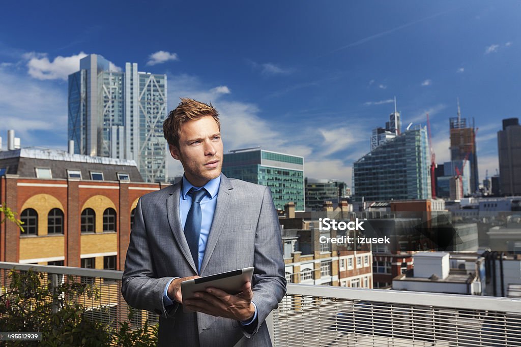 Businessman with digital tablet Portrait of professional businessman standing outside against cityscape with digital tablet, looking away. Adult Stock Photo