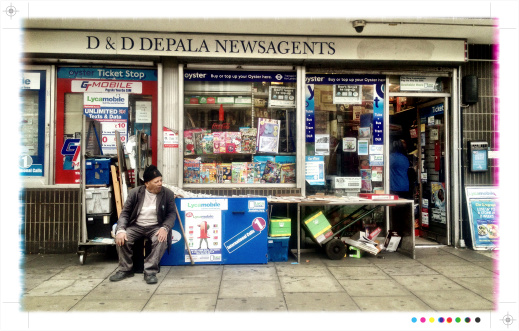 London, UK - September 12, 2013: The shop front to a typical London newsagents store on Holloway Road, north London. The old man sitting outside the shop is waiting to sell papers to passers-by.