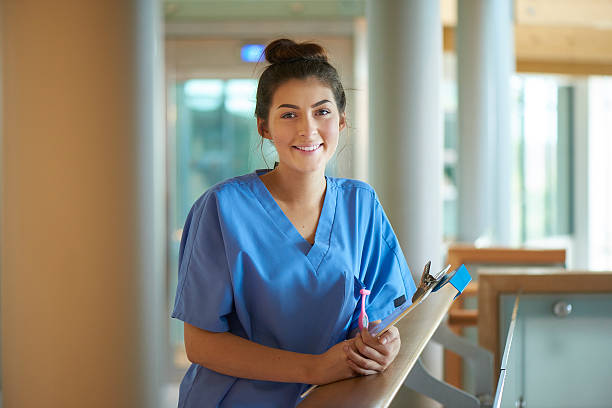 young female nurse in the hospital . a young  female nurse stands proudly on the hospital corridor . She is wearing scrubs and holding a medical records clipboard . female nurse photos stock pictures, royalty-free photos & images