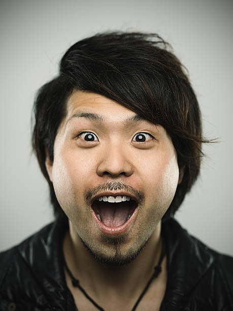 Portrait of a young happy japanese man looking at camera Studio portrait of a happy japanese young man looking at camera with relaxed happy expression and nice smile. The man has around 30 years and has long black hair and casual clothes. Vertical color image from a medium format digital camera. Sharp focus on eyes. mouth open human face shouting screaming stock pictures, royalty-free photos & images