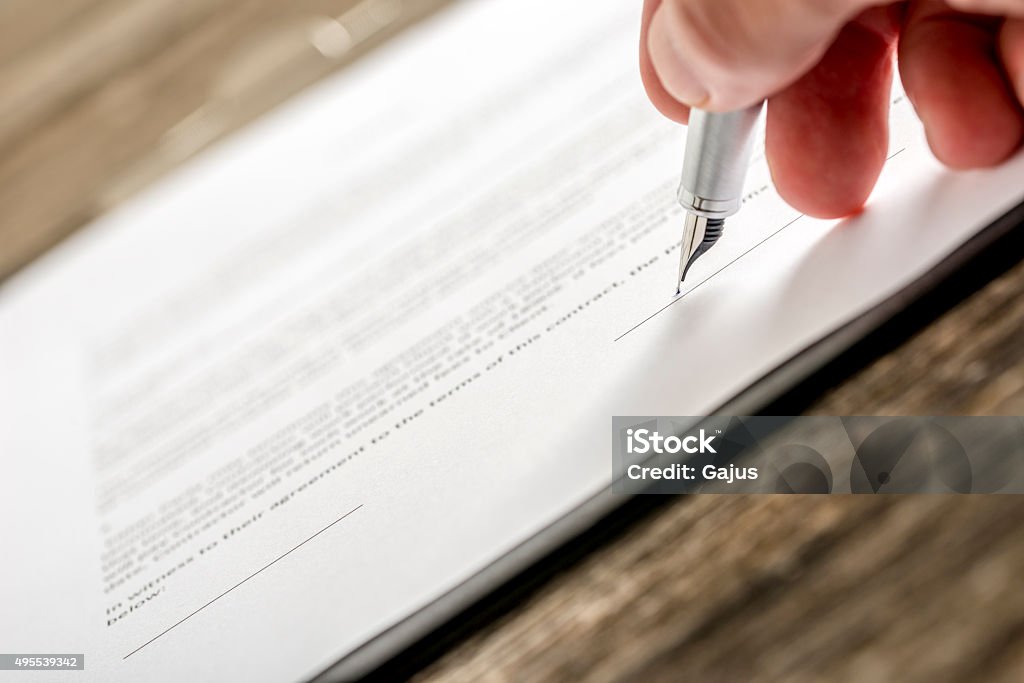 Man signing business document, subscription form or insurance pa Man signing business document, application, subscription form  or insurance papers with silver pen on wooden desk. Contract Stock Photo