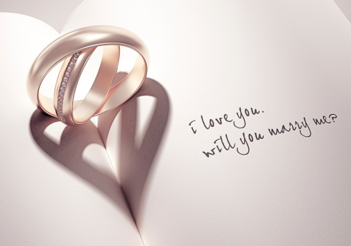 abstract wedding rings with heartshadow on a book middle with i love you will you marry me card text
