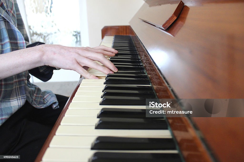 Image of teenage boy playing the piano, wooden piano keyboard Photo showing the hands of a teenage boy playing the piano keyboard, on a traditional wooden piano - practicing some of his favourite music. Arts Culture and Entertainment Stock Photo