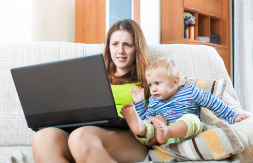 Whiner young mother with a crying baby, working on the Internet with a laptop in the house