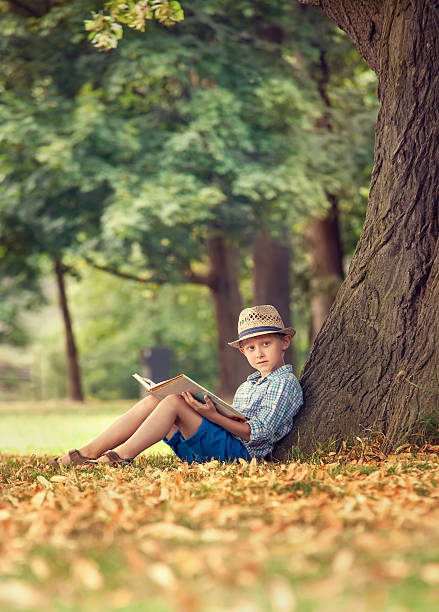 istock Boy with book sitting under big tree in park 495557798