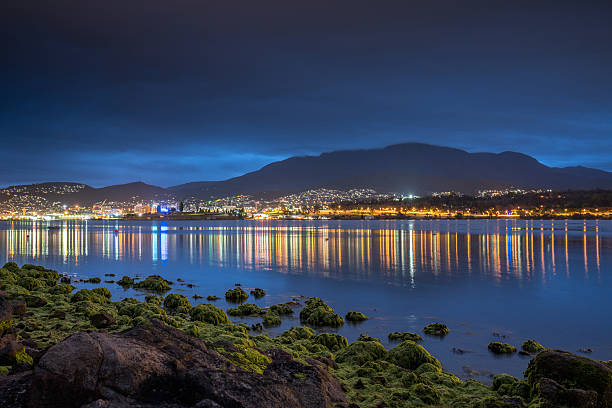 City lights of the skyline of Hobart, Tasmania mirroring on the sea at Night. Hobart, Tasmania, Australia.
