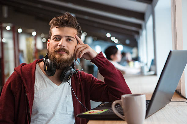 Young confident guy working in office using headset and laptop Young handsome confident guy in brown hoodie working in office using headset and laptop nerd stock pictures, royalty-free photos & images