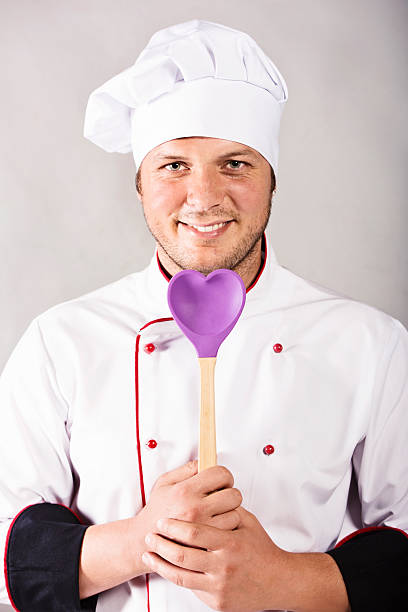 Happy young chef holding heart shaped spoon and smiling