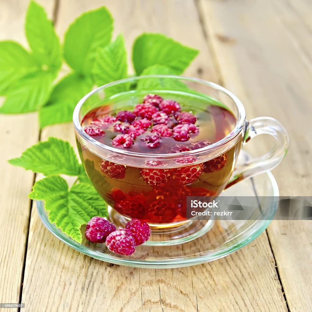 Tea with raspberries in glass cup on board Tea with raspberries in a glass cup, raspberry leaves on the background of wooden boards Berry Fruit Stock Photo