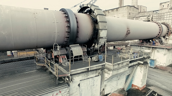 At cement factory. Worker standing near rotary kiln tube