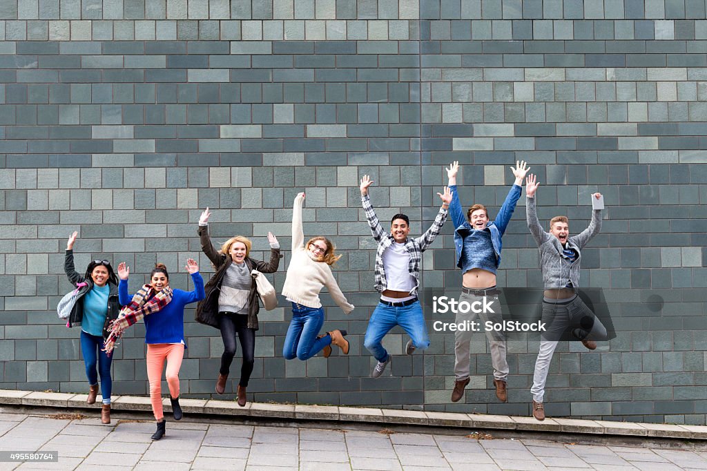 We've passed! Group of young students jumping in the air in celebration. A large grey wall of their college building is behind them. Jumping Stock Photo