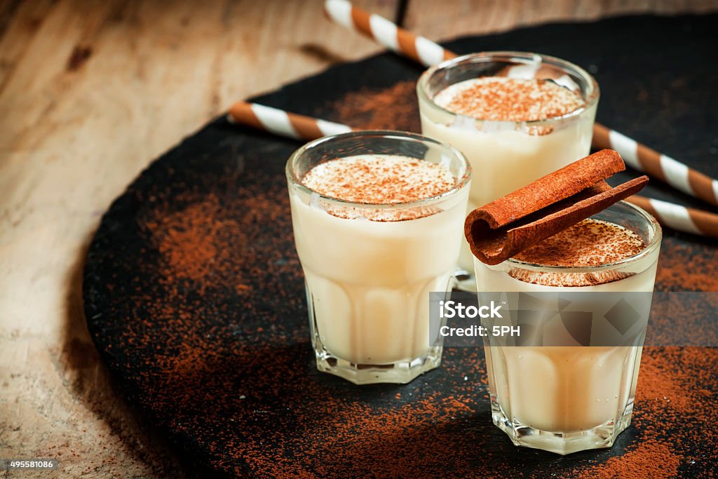 Traditional winter eggnog  with milk, rum and cinnamon Traditional winter eggnog  with milk, rum and cinnamon, sprinkle with grated nutmeg, selective focus Eggnog Stock Photo