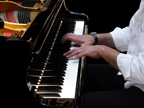 Close-up of pianist's hands during a concert of classical jazz music with a grand coda piano on black background.