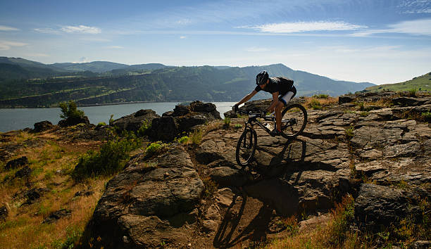 Mountainbiker going down on Little Moab rocks Mountain Biker going downhill on steep rocky trail - Syncline with Cascade Range and Mt Hood view at a background, Columbia River, WA, Oregon, United States syncline stock pictures, royalty-free photos & images