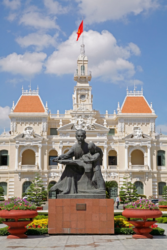 The famous statue of Ho Chi Minh (Bac Ho) holding a small child, standing in front of the impressive French-designed People's Committee Building also known as the City Hall and Hotel de Ville in the centre of Saigon.  The Vietnamese flag is flying on top of the building.