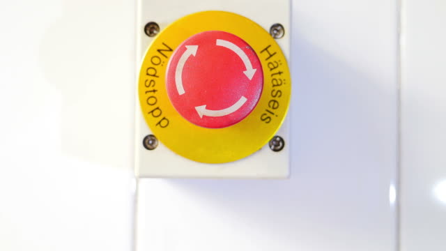 Close up view of an emergency stop button and a hand hitting it