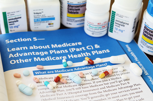 West Palm Beach, USA - October 13, 2015: A US government publication that explains Medicare benefits, titled Medicare and You, lies on a desk. The booklet is open to a page describing Medicare Advantage Plans. Prescription bottles containing various prescription drugs for high blood pressure and cholesterol are grouped on the publication. Various medicines in tablet and capsule form are also on top of the booklet.
