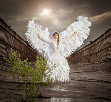 Beautiful angel girl spreading her arms with wings on an abandoned roof