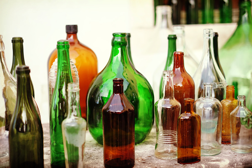 Colourful, old, empty glass bottles in green, brownand transparent that are standing on a table in an market place.