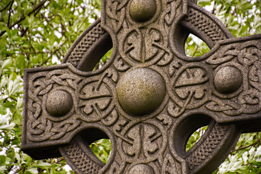 Close-up of an Irish Celtic cross made of stone, to be placed on a tomb,The intricate details of the carving can be seen, showcasing the skill and artistry of the stonemason who crafted it. The cross stands tall and proud, symbolizing the deep cultural and religious roots of Ireland. The texture of the stone adds to the overall aesthetic, creating a sense of timelessness and history. It is a beautiful and meaningful tribute to those who have passed, and a testament to the enduring traditions of Irish heritage
