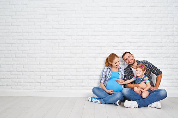 Happy family father and pregnant mother and child daughter near Happy family father and pregnant mother and child daughter near a blank brick wall in the room family photo on wall stock pictures, royalty-free photos & images
