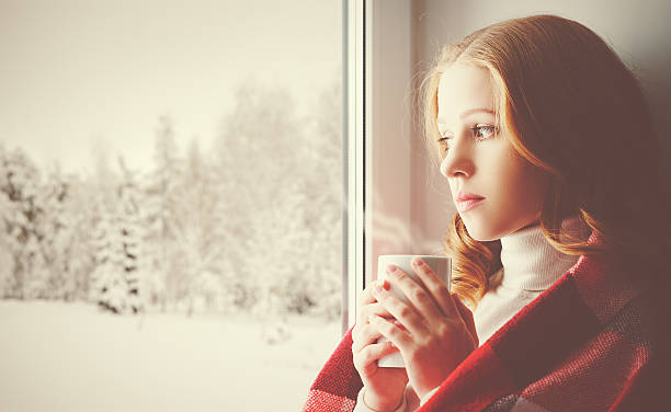 istock Pensive sad girl with a warming drink looking out window 495616508