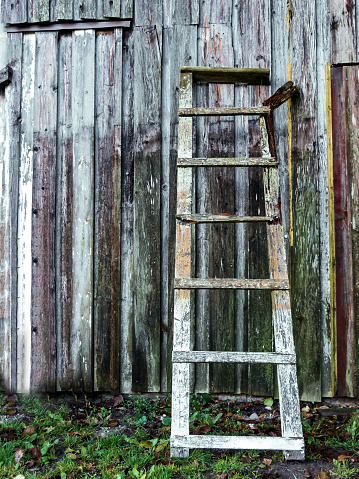 Old hand crafted and slightly broken wooden ladder leaning against a barn wall