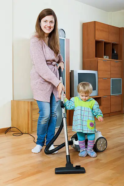 Young mother with her child doing home cleaning with a vacuum cleaner