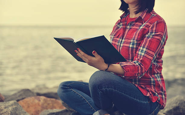 istock girl sitting on rock and reading a book 495627296