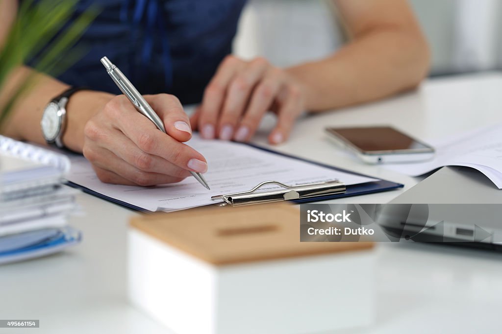 Close-up of female hands working at office Close-up of female hands. Woman writting something and looking at mobile phone screen sitting at her office Privacy Stock Photo