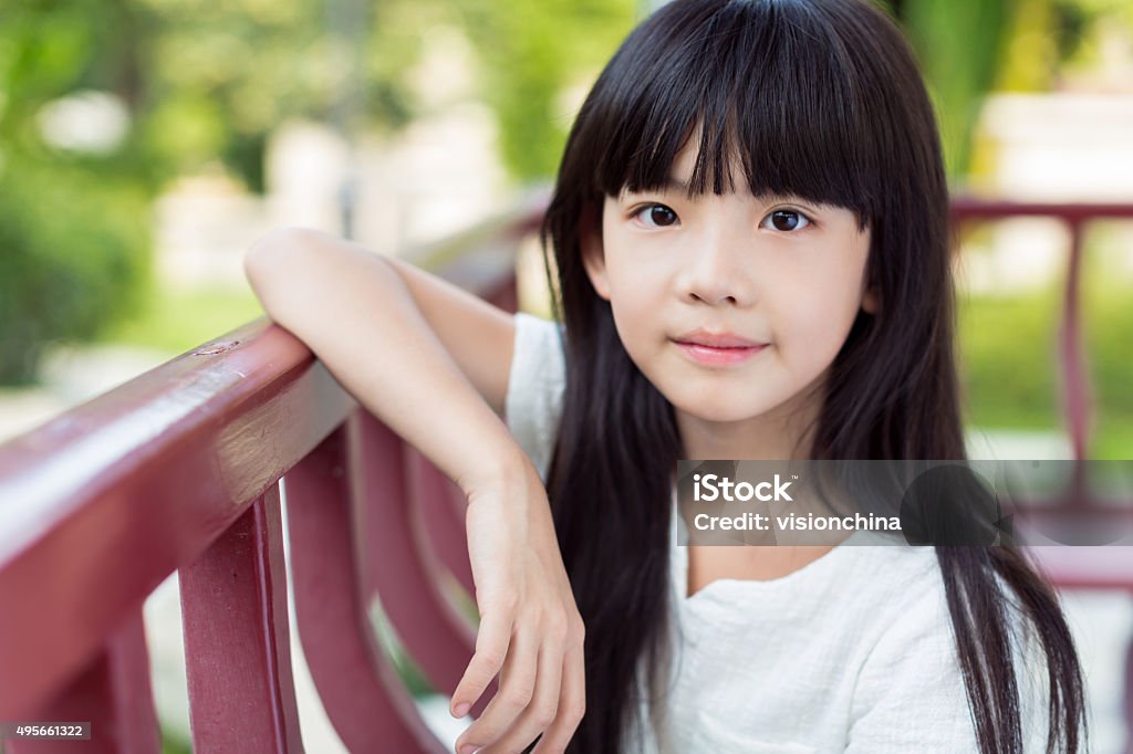 girl sitting on a chair chinese lovely little girl, sitting on a park bench play game and rest 2015 Stock Photo