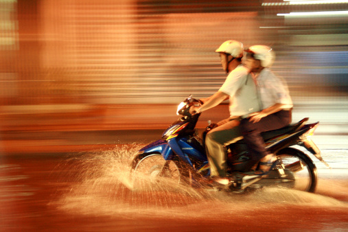 Ho Chi Minh City, Vietnam - October 15, 2009: This photo shows two Vietnamese men riding a motorbike on a flooded street at night during the monsoon season. Blurred motion through panning technique.