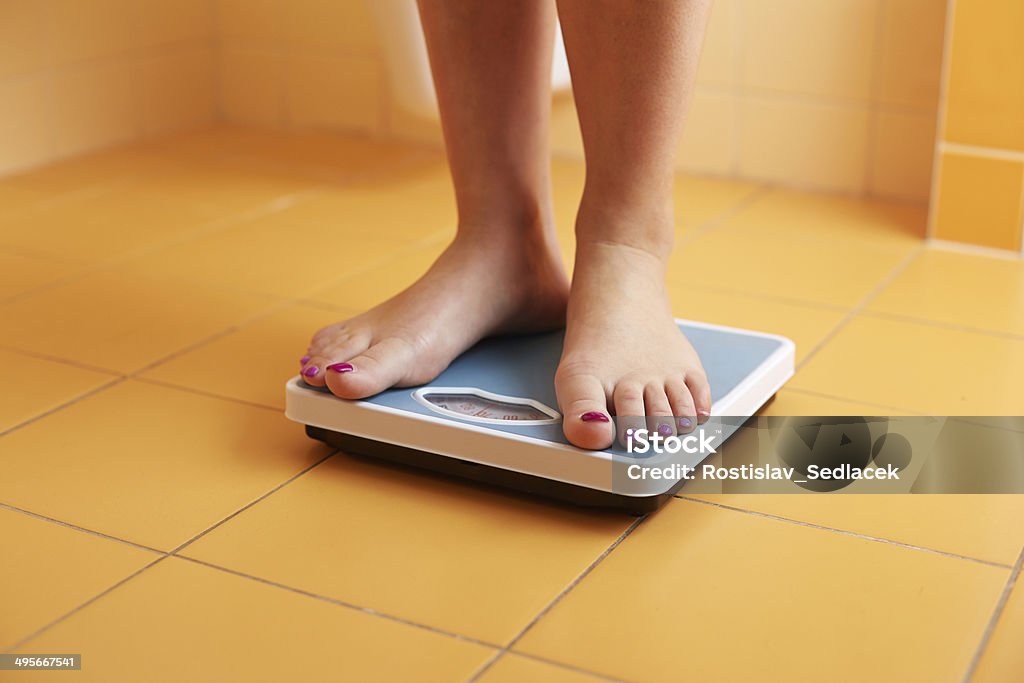 Pair of female feet on a bathroom scale A pair of female feet standing on a bathroom scale Weight Scale Stock Photo