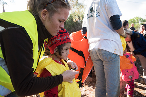 Skala Sikamineas, Lesbos, Greece - October 25, 2015: A Norwegian volunteer assists a little girl in removing her life jacket after an overcrowded rubber dingy carrying refugees and other migrants landed on the Greek island of Lesbos, near the town of Skala Sikamineas. The boat had traveled the 10 kilometer distance from Turkey.