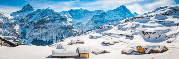 Winter wonderland wooden ski chalets Alpine village snowy mountain peaks Traditional wooden chalets high in the Alps buried under crisp white snow below mountain peaks. ProPhoto RGB profile for maximum color fidelity and gamut. grindelwald photos stock pictures, royalty-free photos & images
