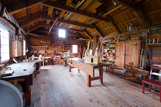 Carpentry with tools and wood workpieces Interior carpentry workshop with workbench, tools hanging on the wooden walls, wooden blank and finished carpentry. Indoor dried planks on wooden beams overlap workshop. Shop lit with natural light from two small windows. drudgery photos stock pictures, royalty-free photos & images