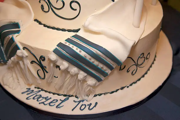 Blue and white Bar Mitzvah cake with tallis decoration and Mazel Tov written on it.