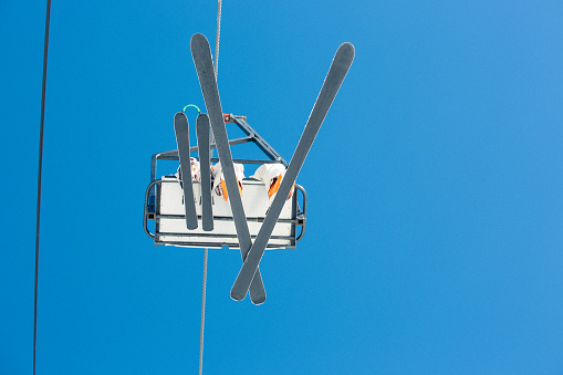 Unrecognizable adult and child in a chairlift with blue sky in the background. The chairlift is right over head and gives an unusual perspective.