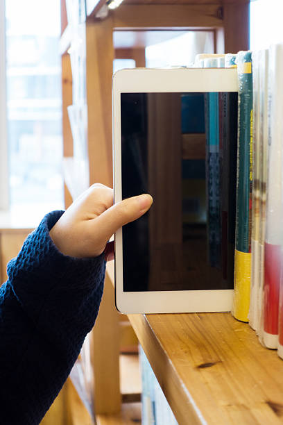 Woman hand choosing tablet from a bookshelf stock photo