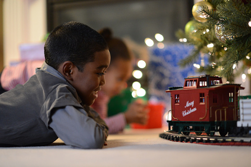 A little boy playing with a newly opened train set on Christmas morning in his families living room.