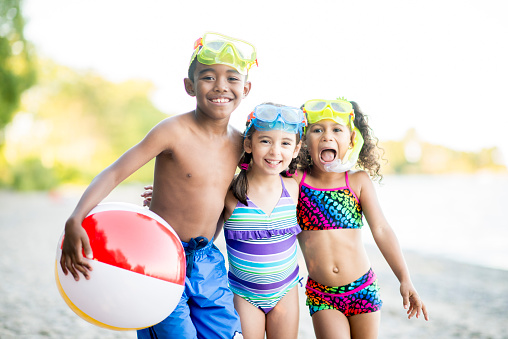 A multi-ethnic group of children on a beach in their swimsuits with snorkel gear playing with a beach ball.