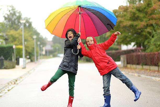 Two happy school boys sharing colorful umbrella