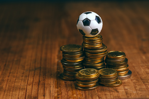 Soccer bet concept with small football on top of coin stack, making money by predicting sport results.