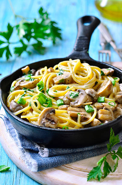 Spaghetti with mushroom and green onion in cream on turquoise wooden table.